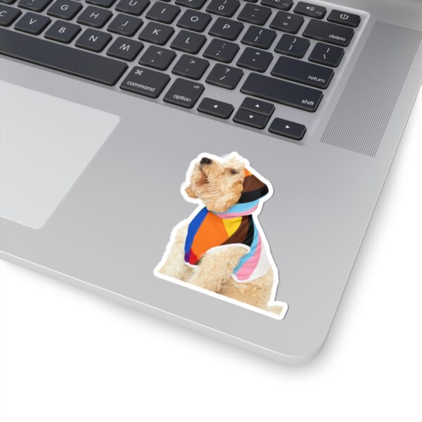Kiss cut sticker of a dog wearing Pride gear, with the sticker cut around the dog’s outline and a peelable backing sheet behind it.